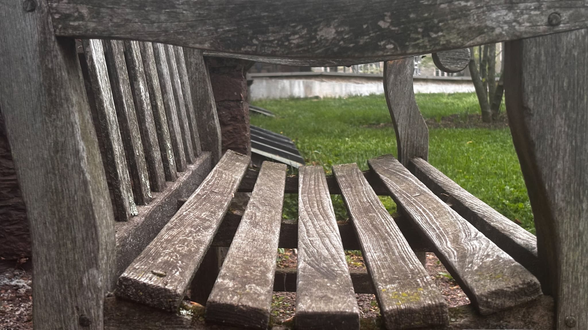 Unedited Weathered wooden bench photographed from underneath with green grass beyond it